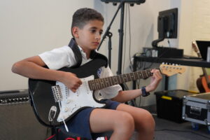 Gallery - Gallery Music School. Image of a boy playing the guitar in a music lesson, showcasing his talent and dedication as he strums the guitar strings with skill and enthusiasm, guided by his music teacher. Guitar classes Adelaide, Adelaide guitar lessons, guitar instruction Adelaide, Adelaide guitar teacher, guitar classes in Adelaide, guitar teacher Adelaide, guitar lessons Adelaide, Adelaide guitar instructor, guitar lessons in Linden Park SA.